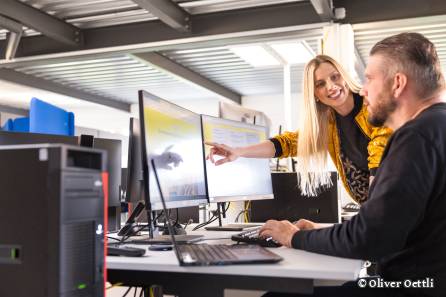 Mitarbeiterin zeigt Kollege etwas auf Bildschirm